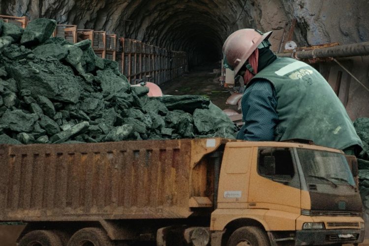 A worker in a hard hat handles extracted minerals beside a loaded truck inside a mining tunnel in Afghanistan. (Photo credit: Exclusive + Pexels)