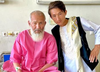 Esmat Khan Amiri sits with his father in a hospital ward amid allegations that he was denied surgery at a Kandahar hospital due to ethnic discrimination. (Photo credit: social media)