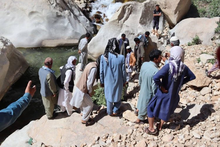 A crowd of people gathered near the water in Daikundi province following a drowning incident, as locals observed the scene while search efforts continued. (Photo credit: RTA Daikondi)