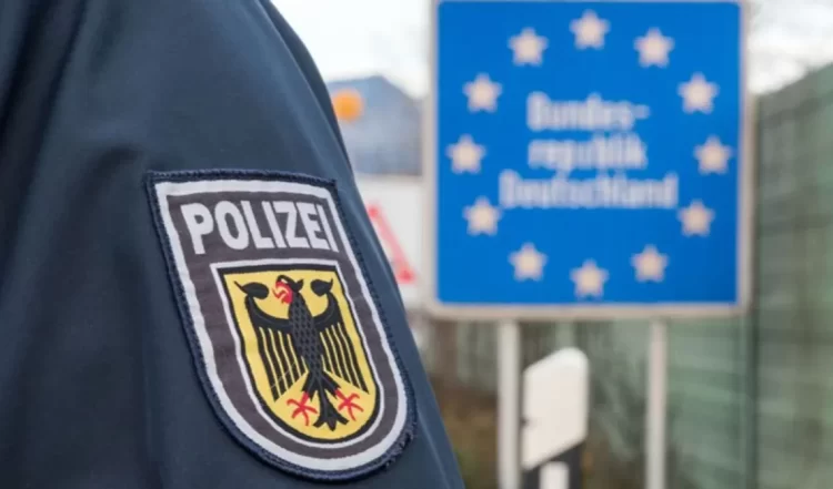 German police officer's uniform displays 'POLIZEI' patch with federal eagle in front of EU Germany sign at border area. (Photo credit: Logos press)