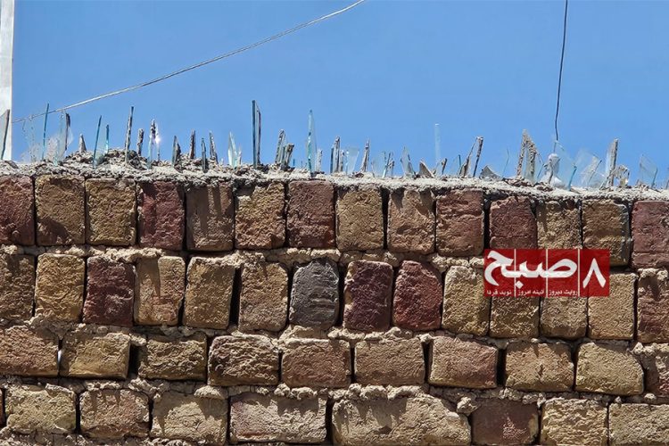 Sharp glass shards embedded in cement line the top of a stone yard wall in Kabul, a traditional security measure residents have increasingly turned to as burglaries surge across the city. (Photo credit: 8am.media)