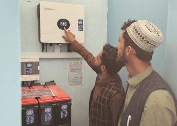 Two individuals inspecting and operating a solar power system and battery storage units supported by the United Nations Development Programme (UNDP), an initiative aimed at expanding access to sustainable energy and strengthening local power infrastructure. (Photo credit: UNDP)