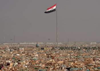 The Iraqi flag flies over a densely populated urban landscape, as Iran's Revolutionary Guard announces strikes against armed groups in the country's north. (Photo credit: QASSEM AL-KAABI / AFP)