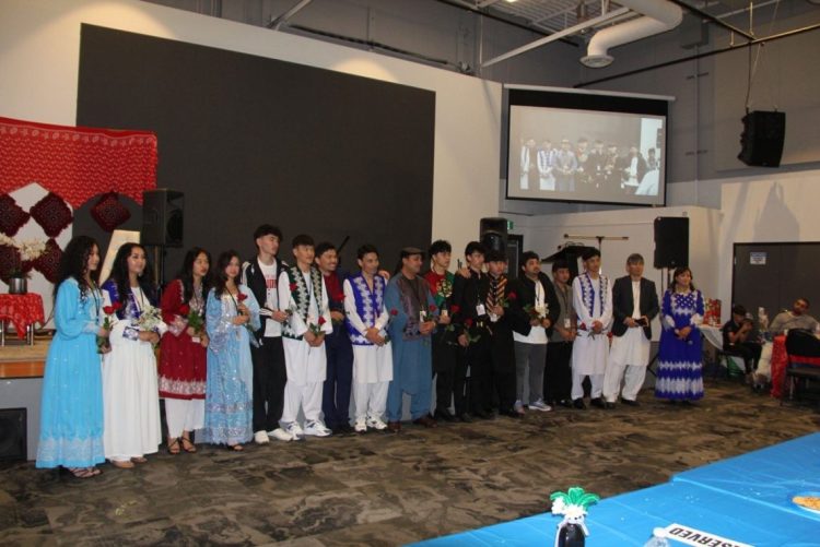 Participants in traditional Hazara attire line up on stage during the Hazara Culture Day ceremony held in Calgary, Canada. (Photo Credit: Exclusive)
