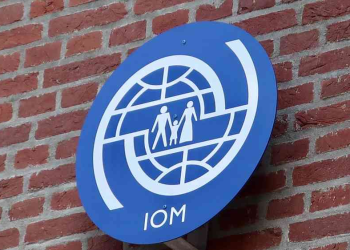 The logo of the International Organization for Migration (IOM) is seen on the wall of one of this agency’s offices, an organization that works in the field of assisting migrants and providing humanitarian services. (Photo Credit: Shutterstock / DCStockPhotography)