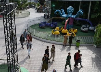 Families walk through a Kabul amusement park as a Talib stands among the visitors, amid sweeping Taliban restrictions on women's access to recreational spaces. (Photo credit: AFP)