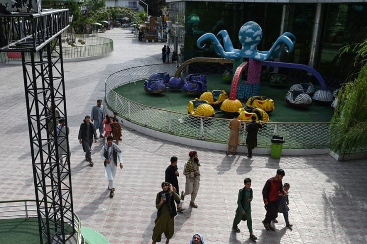 Families walk through a Kabul amusement park as a Talib stands among the visitors, amid sweeping Taliban restrictions on women's access to recreational spaces. (Photo credit: AFP)
