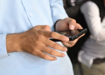 A man uses his mobile phone in a public setting in Nangarhar, where residents report repeated phone searches by Taliban members. (Photo credit: AFP)
