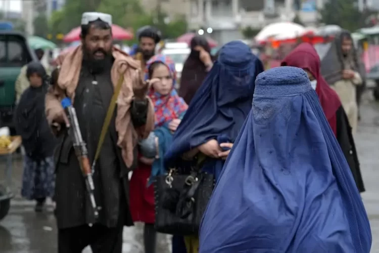 A Taliban fighter carrying a rifle stands among women in burqas at a market in Afghanistan. (Photo credit: AP)