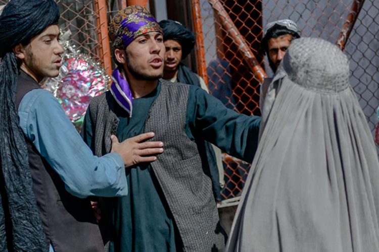 Men gather on a street in Afghanistan as a burqa-clad woman stands nearby, reflecting the tightly controlled public life under Taliban rule. (Photo Credit: AFP)