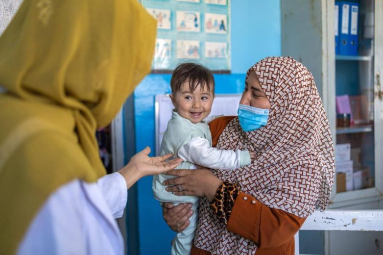 A female health worker receives a smiling infant at a UNICEF-supported health center in Afghanistan, where female vaccinators remain essential to child immunization services. (Photo credit: @TajudeenOyewale)