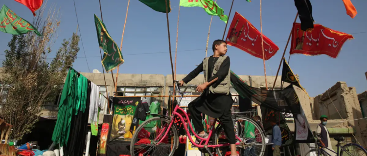 A boy rides a bicycle past Ashura mourning flags and banners displayed for Muharram commemorations in Kabul. (Photo credit: Rahmat Gul/AP)