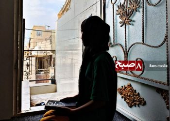 A schoolgirl sits at the entrance of her home holding books, reflecting on the continued closure of girls' schools in Afghanistan. (Photo credit: 8am.media)