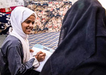 A young girl smiles while writing in a notebook during a home based lesson, as girls across Afghanistan remain barred from formal education. (Photo credit: UNICEF)