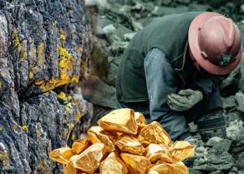 A miner works near a rock face as piles of gold nuggets sit in the foreground, symbolizing Afghanistan's contested gold mining industry. (Photo credit: Pexels + Freepik)