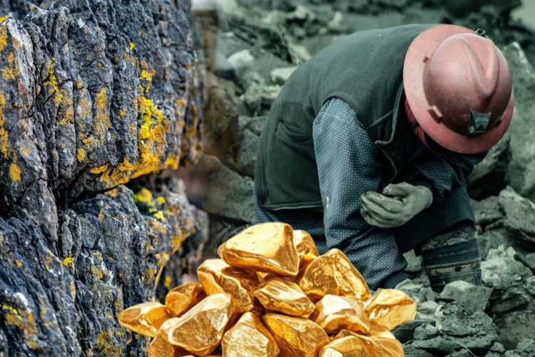 A miner works near a rock face as piles of gold nuggets sit in the foreground, symbolizing Afghanistan's contested gold mining industry. (Photo credit: Pexels + Freepik)