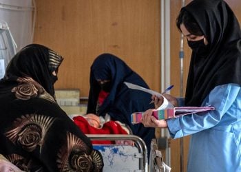 A nurse reviews medical records as women wait beside a patient's bed at a hospital in Herat. (Photo credit: AFP)