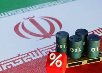 Miniature oil barrels are displayed in front of the Iranian flag, illustrating the decline in oil prices following the halt in reciprocal attacks between the United States and Iran. (Photo credit: Reuters)