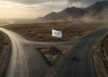 A Taliban flag stands at a crossroads on a newly built highway in Afghanistan, symbolizing the debate over the true purpose of the group's road construction projects. (Photo credit: AI)