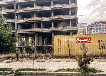 An unfinished residential building sits behind a shipping container in Kabul as rising material costs halt construction projects. (Photo credit: 8am.media)