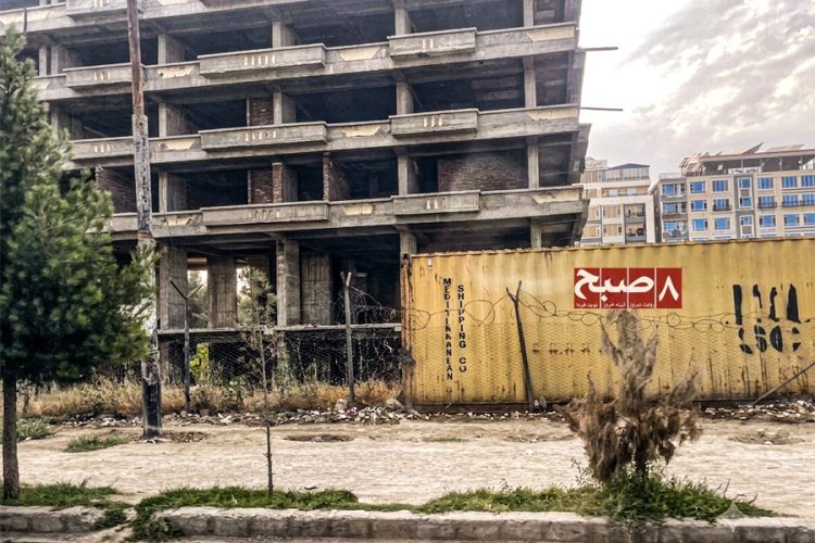 An unfinished residential building sits behind a shipping container in Kabul as rising material costs halt construction projects. (Photo credit: 8am.media)