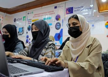 Three girls wearing hijabs and face masks are seen working on computers at a training center. The United Nations Development Programme (UNDP) says that part of its European Union-funded development projects in Badakhshan focuses on empowering women and young people through technical and vocational skills training. (Photo credit: UNDP)