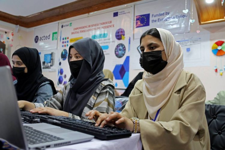 Three girls wearing hijabs and face masks are seen working on computers at a training center. The United Nations Development Programme (UNDP) says that part of its European Union-funded development projects in Badakhshan focuses on empowering women and young people through technical and vocational skills training. (Photo credit: UNDP)