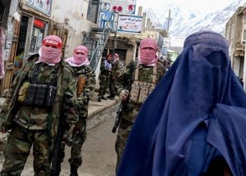 Taliban fighters patrol a street as an Afghan woman wearing a burqa walks past in a mountainous area of Afghanistan (Photo: Wakil KOHSAR / AFP)