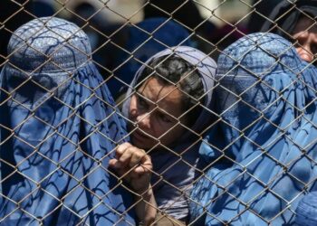 Afghan women and a child stand behind a wire fence, reflecting the barriers, restrictions, and hardships faced by women and girls in Afghanistan (Photo: Getty Images)