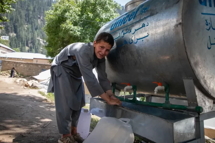 A boy collects water from a UNICEF water tank in Afghanistan following recent floods. (Photo credit: UNICEF)