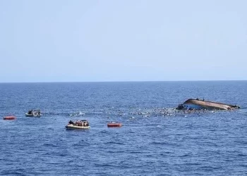 Rescue teams search the waters after a boat carrying migrants capsized, with survivors and rescuers visible near the overturned vessel