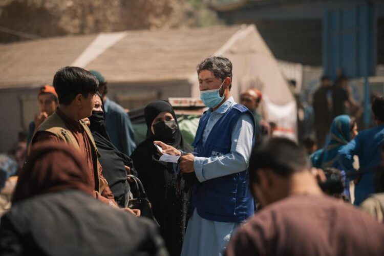 People gather around an IOM employee holding a note during the delivery of humanitarian assistance to returnees in Afghanistan. (Photo credit: IOM)
