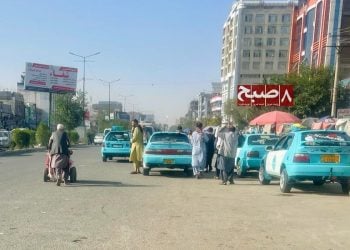 Taxi drivers and pedestrians gather along a Kabul street as vehicles wait near a designated stop. (Photo credit: 8am.media)