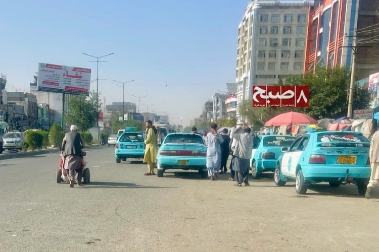 Taxi drivers and pedestrians gather along a Kabul street as vehicles wait near a designated stop. (Photo credit: 8am.media)