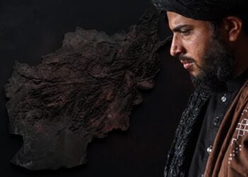 A Talib official gazes downward beside a textured relief map of Afghanistan, symbolizing the country's uncertain path under continued Taliban rule. (Photo credit: AFP)