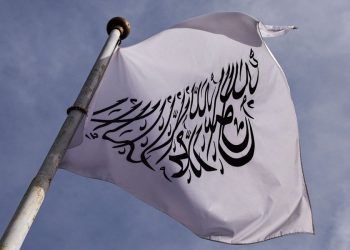 A Taliban flag bearing Islamic calligraphy flutters against a cloudy sky atop a metal pole. (Photo credit: Reuters)