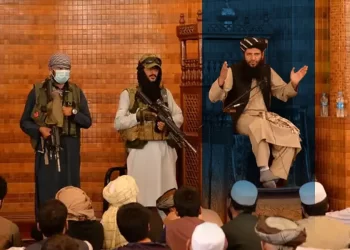 A Taliban mullah delivers a Friday sermon inside a mosque as armed fighters stand guard nearby. (Photo credit: DW)