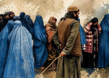 Women wait in line behind a Taliban fighter as morality police enforce dress and movement restrictions across Afghanistan. (Photo credit: AFP)