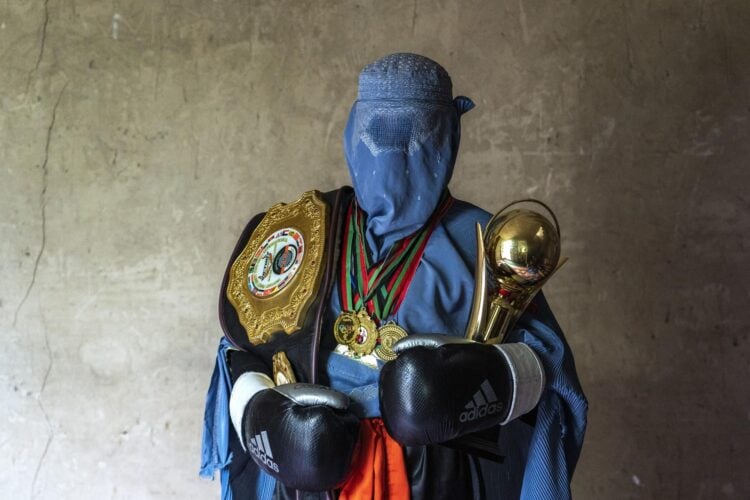 An Afghan female boxer poses with her championship belt, trophies, and medals, celebrating her achievements in the sport in a blue burqa (Photo: AP / Ebrahim Noroozi)