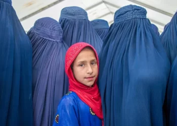 A girl stands among women wearing blue burqas in Afghanistan amid concerns over women’s rights and restrictions. (Photo credit: UN)