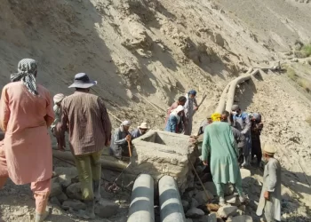 Workers repair a damaged water pipeline in a dry, rugged area.