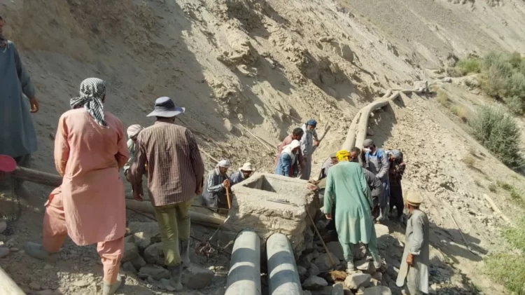 Workers repair a damaged water pipeline in a dry, rugged area.
