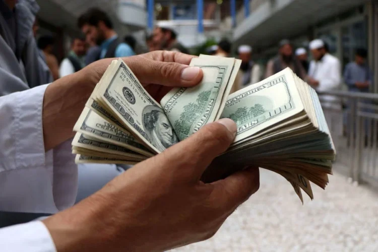 A person counts a stack of US dollar banknotes as people stand in the background, amid banking restrictions that keep citizens and traders reliant on exchange shops. (Photo credit: Reuters)