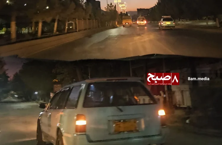 Vehicles travel along a road in Kabul at dusk, with headlights illuminating the streets as night falls.