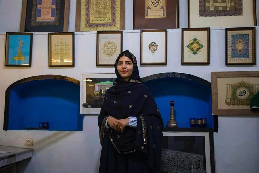 A young woman stands before calligraphy and miniature artworks at Naiko Arts, an institute for girls in Herat. (Photo credit: Exclusive)
