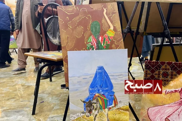 Paintings by young artists, including a woman in a blue burqa leading a donkey, are displayed on easels at an art exhibition in Afghanistan. (Photo credit: 8am.media)