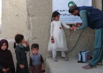 A health worker administers a polio vaccine to a young girl as other children wait nearby (Photo: @PolioFreeAfghan)