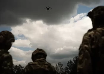 Soldiers look up at a drone flying overhead against a cloudy sky (Photo: GETTY IMAGES)