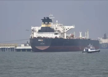 A large oil tanker is docked at a port near the Strait of Hormuz, with a small vessel sailing nearby (Photo: AA)