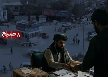 A Taliban official hands cash to a man at a desk stacked with aid boxes and documents in Kunduz. (Photo credit: 8am.media + AI)